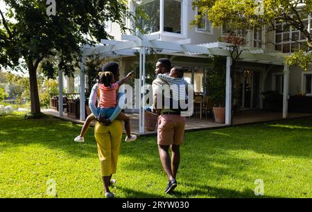 Vista posteriore di madre e figlia afroamericana che sostengono i bambini nel cortile esterno della casa Foto Stock