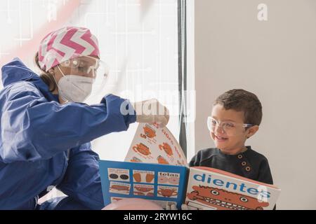 Questa foto mostra un uomo che aiuta un bambino a leggere un libro mentre indossa una maschera facciale Foto Stock