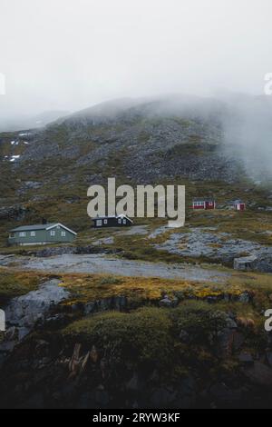 Le cabine in legno si stagliano su uno sfondo di aspre cime montuose coperte da nuvole voluminose Foto Stock