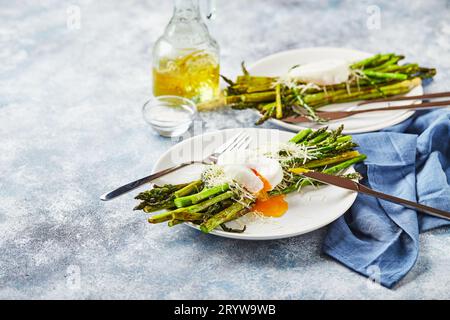 Asparagi verdi con uova in camicia e parmigiano, colazione vegetariana servita su due piatti bianchi su sfondo chiaro. Foto Stock