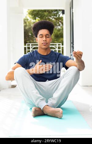 Rilassato uomo birazziale che pratica meditazione yoga seduto sul balcone Foto Stock