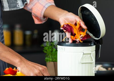 Parte centrale dell'uomo birazziale che indossa il grembiule che prepara il pasto, compostando rifiuti vegetali in cucina Foto Stock