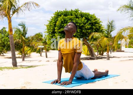 Uomo birazziale concentrato che pratica yoga, si allunga sul tappetino sulla spiaggia soleggiata, inalterato Foto Stock