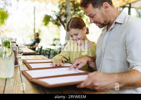 Padre e figlia leggono i menu in un ristorante, scegliendo cibo e bevande. Foto Stock