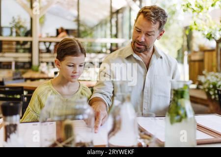 Padre e figlia leggono i menu in un ristorante, scegliendo cibo e bevande. Foto Stock