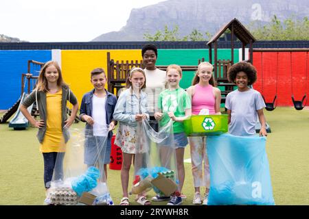 Ritratto di educatrici e alunne felici e diversificate che svolgono attività di riciclaggio raccolte nel cortile scolastico Foto Stock