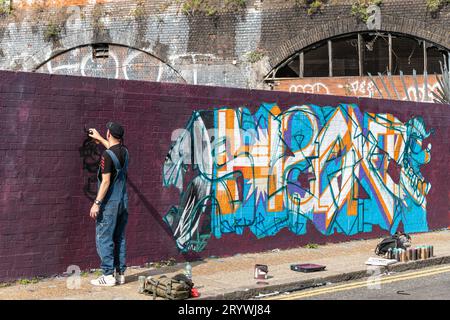 Uno spray di graffiti dipinge un muro a Braithwaite St Shoreditch, Londra, E1. Foto Stock