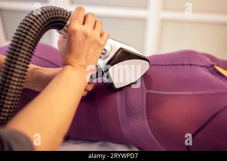 Cosmetico senza volto che utilizza un apparecchio dimagrante a GPL sul corpo di una cliente femminile Foto Stock