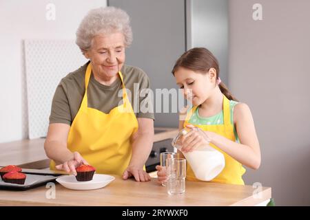 Donna anziana e sua nipote versano latte nel bicchiere in cucina Foto Stock