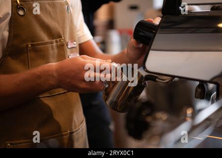 Immagine ritagliata del latte del barista per preparare il latte al bar Foto Stock