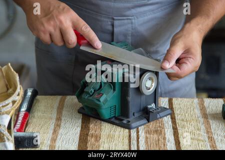 Immagine di un calzolaio che affina un coltello da cucina con una rotella per affilare. Foto Stock