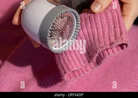 Donna che usa un rasoio anti-pilling a casa. Dispositivo per la rasatura degli abiti. Rasoio in tessuto anti-peluche. Pillola maglione portatile elettrica def Foto Stock