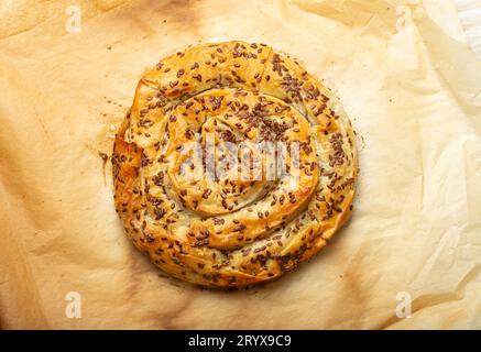 Buccia appena sfornata in pasta filo con ripieno su sfondo di carta da forno vista dall'alto. Tradizionale torta a spirale salata dei Balcani, del Medio Oriente e. Foto Stock
