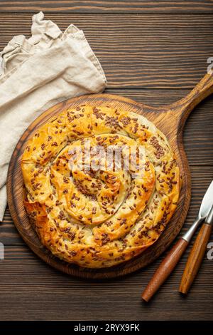 Buccia realizzata con pasta phyllo con ripieno su tagliere, vista dall'alto su sfondo rustico in legno marrone scuro. Tradizionale torta a spirale salata dei Balcani Foto Stock