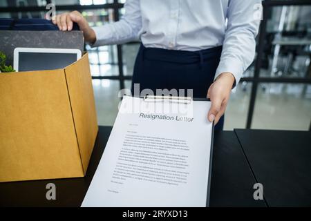 Donna d'affari che invia una lettera di dimissioni al capo e che tiene in mano le cose rassegnate deprimere o che porta una scatola di cartone alla scrivania in ufficio Foto Stock