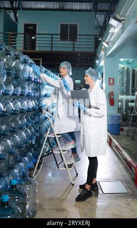 Ritratto di uno scienziato nella fabbrica di acqua potabile usando una scala, guardando i serbatoi dell'acqua sopra ed esaminando con un coll Foto Stock