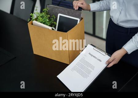 Donna d'affari che invia una lettera di dimissioni al capo e che tiene in mano le cose rassegnate deprimere o che porta una scatola di cartone alla scrivania in ufficio Foto Stock