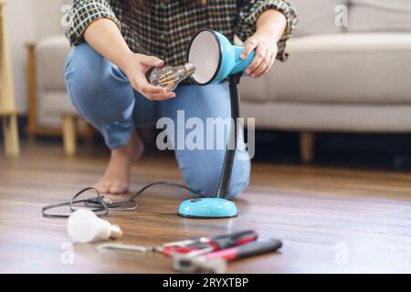 Donna asiatica che cambia la lampadina nel rinnovamento della lampada utilizzando attrezzature per la riparazione fai-da-te della lampadina e della lampada seduto sul pavimento Foto Stock