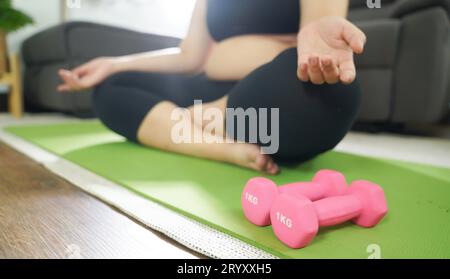 Donna in sovrappeso che si esercita per perdita di peso. Allenati con i manubri in posizioni strette a casa tua in salotto allegramente Foto Stock