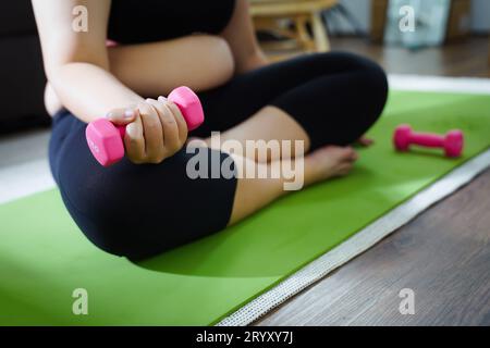 Donna in sovrappeso che si esercita per perdita di peso. Allenati con i manubri in posizioni strette a casa tua in salotto allegramente Foto Stock