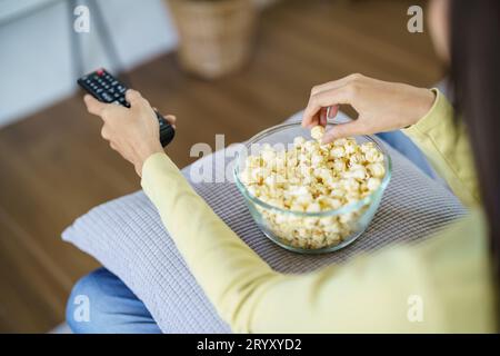Donna asiatica che guarda la Smart TV e utilizza il telecomando tenendo il telecomando audio della televisione a casa con il telecomando Foto Stock