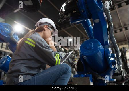 Un ingegnere donna installa un programma su un braccio robotico in un magazzino robot. E provare il funzionamento prima di inviare la macchina Foto Stock