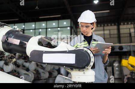 Un ingegnere donna installa un programma su un braccio robotico in un magazzino robot. E provare il funzionamento prima di inviare la macchina Foto Stock