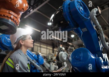 Un ingegnere donna installa un programma su un braccio robotico in un magazzino robot. E provare il funzionamento prima di inviare la macchina Foto Stock