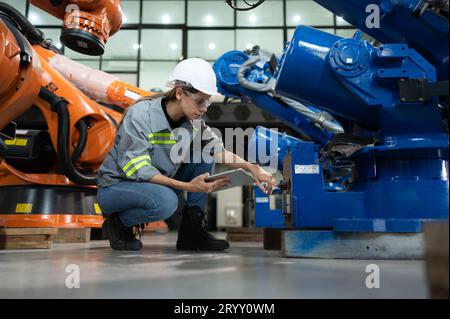 Un ingegnere donna installa un programma su un braccio robotico in un magazzino robot. E provare il funzionamento prima di inviare la macchina Foto Stock