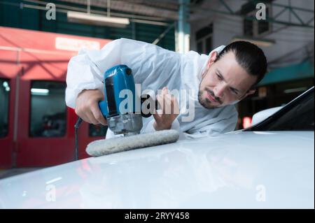 Il meccanico automatico utilizza una lucidatrice elettrica per lucidare la vernice essiccata dell'auto. Dopo aver passato la vernice dalla sala di verniciatura dell'auto Foto Stock