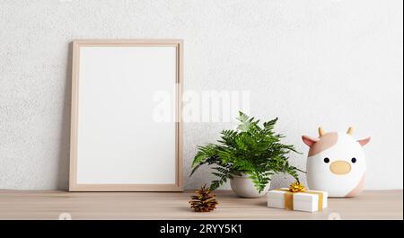 Mockup con cornice fotografica vuota su tavolo di legno con bambola mucca pianta di pino e confezione regalo. Arte e decorazione. Illustrazione 3D. Foto Stock