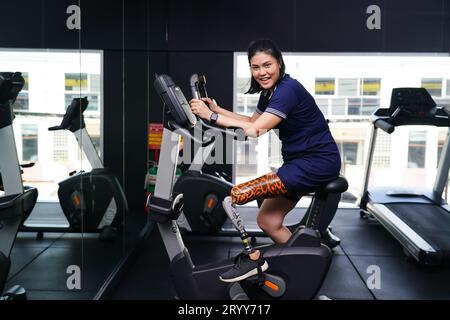 Giovane donna con una gamba protesica con esercizio con una bicicletta spinning in palestra per praticare l'uso articolare con l'altra gamba normale per essere flessibile, C Foto Stock