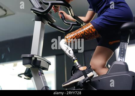 Giovane donna con una gamba protesica con esercizio fisico con una bicicletta spinning in palestra per praticare l'uso articolare con l'altra normale Foto Stock