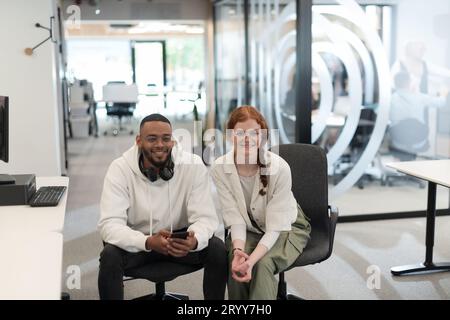 In un ufficio moderno, il giovane uomo d'affari afroamericano e la sua collega donna d'affari, con i suoi sorprendenti capelli arancioni, si impegnano Foto Stock