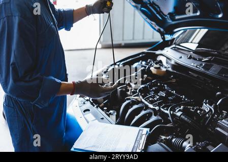 Il meccanico dell'auto che mantiene l'olio per ingranaggi di controllo sul veicolo di manutenzione su ordine del reclamo del cliente nell'officina di riparazione auto. Riparazione del motore Foto Stock