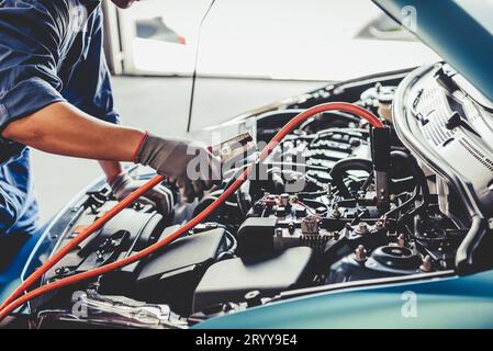 Meccanico dell'auto che tiene i cavi elettrici della batteria ponticello e controlla il veicolo di manutenzione tramite ordine di richiesta di rimborso cliente in aut Foto Stock