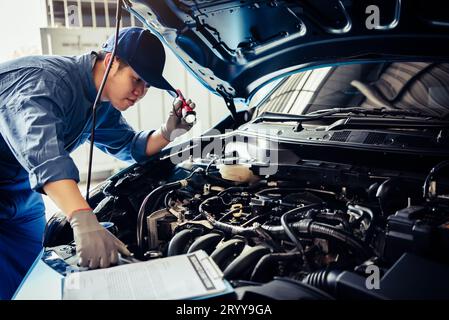 Tecnico meccanico che tiene una torcia elettrica che controlla il motore con la clipboard dell'elenco di controllo sul veicolo di manutenzione in base alla richiesta di rimborso del cliente Foto Stock