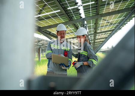 Un team di ingegneri elettrici sta ispezionando e manutenendo i pannelli solari in un sito di pannelli solari nel mezzo di cento acri Foto Stock