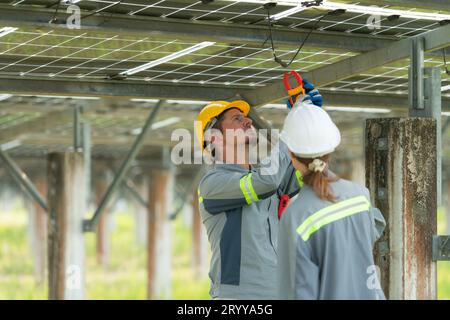 Un team di ingegneri elettrici sta ispezionando e manutenendo i pannelli solari in un sito di pannelli solari nel mezzo di cento acri Foto Stock