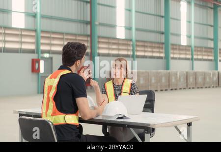 Incontro tra designer e responsabile del magazzino per organizzare la disposizione degli scaffali dei prodotti in un enorme magazzino vuoto. Foto Stock