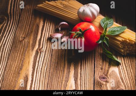 Gustosi e appetitosi spaghetti italiani ingredienti per la cucina con pomodoro, aglio e basilico su tavola marrone di legno. FO Foto Stock