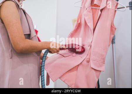 Donna che utilizza il ferro da stiro per stirare la camicia alla moda nella lavanderia. Ragazza che fa ferro vapore per stirare i vestiti in mano. Laun Foto Stock