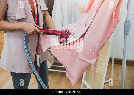 Donna che utilizza il ferro da stiro per stirare la camicia alla moda nella lavanderia. Ragazza che fa ferro vapore per stirare i vestiti in mano. Laun Foto Stock