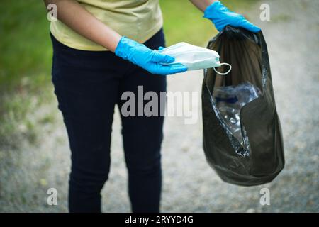 Beneficenza volontaria womanÂ mano che tiene la maschera di protezione chirurgica durante la pandemia di coronavirus. COVID-19. Â gettando via i pezzi usati p Foto Stock