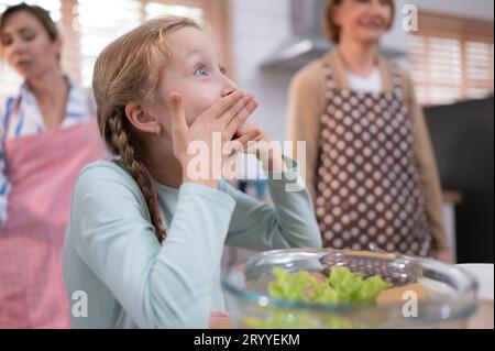 Nipote di nonni in una cucina piena di luce naturale, mangia l'insalata nonna preparata per la cena in famiglia. Foto Stock