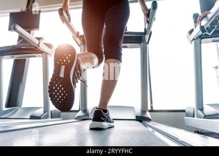 Il corpo inferiore a gambe parte della ragazza di Fitness in esecuzione sulla macchina in esecuzione o il tapis roulant in palestra per il fitness con sun ray. Tono caldo. Una sana e l'attività ginnica Foto Stock