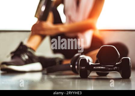 Ravvicinare i manubri con l'esercizio fisico femminile in palestra rompere il fitness rilassarsi dopo l'allenamento sportivo con il biberon di frullato proteico Foto Stock