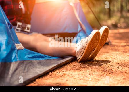 Primo piano di una donna che tiene i piedi con una scarpa con sfondo naturale. Donna turistica che riposa nella tenda del campeggio. Persone e stili di vita Foto Stock