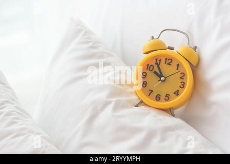 Allarme giallo di clock sul letto bianco sullo sfondo. Viaggi e Vacanze concetto. Home accessori oggetto del tema. Foto Stock