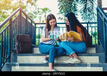 Due ragazze asiatiche di bellezza leggono e insegnano libri per l'esame finale insieme. Studente sorridente e seduto sulle scale. Educatio Foto Stock